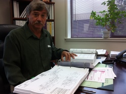 Sitka utility director Chris Brewton, with the hundreds of pages of planning documents for the Blue Lake project. (KCAW photo/Ed Ronco)