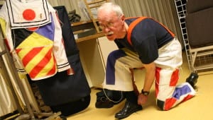 Bill Foster, 74, puts on his wearable art before Wednesday night's dress rehearsal at the Sitka Wearable Arts Show. The title of Foster's outfit is "In the Navy," and is comprised of 13 maritime signal flags attached to a U.S. Navy sailor suit. (Photo by Ed Ronco/KCAW)