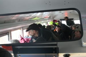 Members of the public are seen in the rear view mirror of a school bus as they peer out the windows at parts of the Blue Lake dam construction site, during a tour on Sunday. (KCAW photo by Ed Ronco)