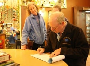 State Sen. Bert Stedman signs his name to a petition to repeal Senate Bill 21, as his wife, Lureen, and daughter Susan look on. If successful, the petition would put the question before voters in August 2014. Organizers must gather more than 30,000 signatures from across the state. (KCAW photo by Ed Ronco)
