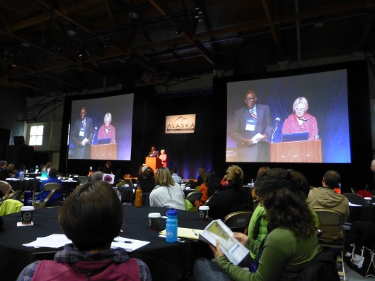 Lenwood Sloan, left on the screens, was keynote speaker at the Alaska Travel Industry Association conference. (Rich McClear/KCAW)