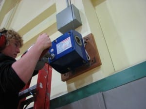 Becker connects the bit to a large drill and inserts it into the winch. The basket goes up to the ceiling in less than a minute. (KCAW photo/Robert Woolsey)
