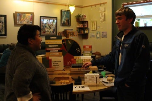 The "balance the budget" game invites Alaskans to set the state on a sustainable financial path. Reid Magdanz looks on as Blossom Twitchell takes a turn. (Emily Kwong/KCAW photo)